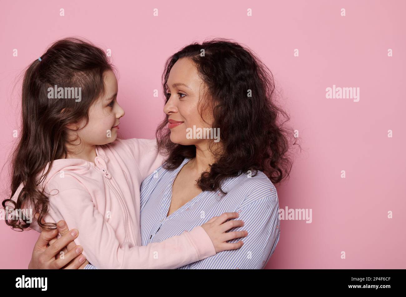 Madre e figlia felici, abbracciandosi, sperimentando la felicità, stando faccia a faccia su sfondo rosa isolato Foto Stock