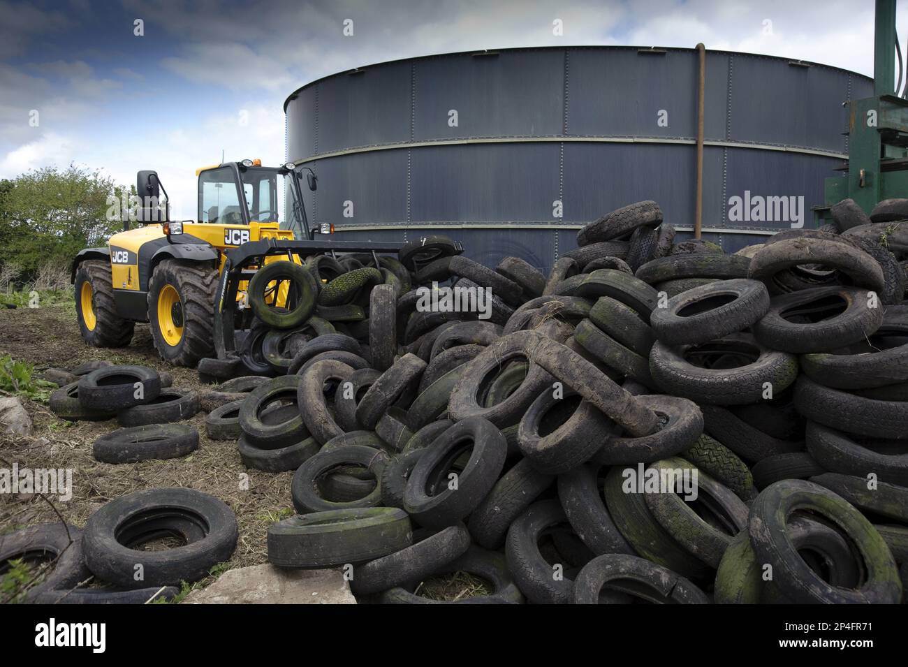 Riciclaggio di pneumatici in gomma, movimentatore telescopico JCB che spinge i pneumatici in cumulo, in azienda agricola vicino a un deposito di liquami, Inghilterra, Regno Unito Foto Stock