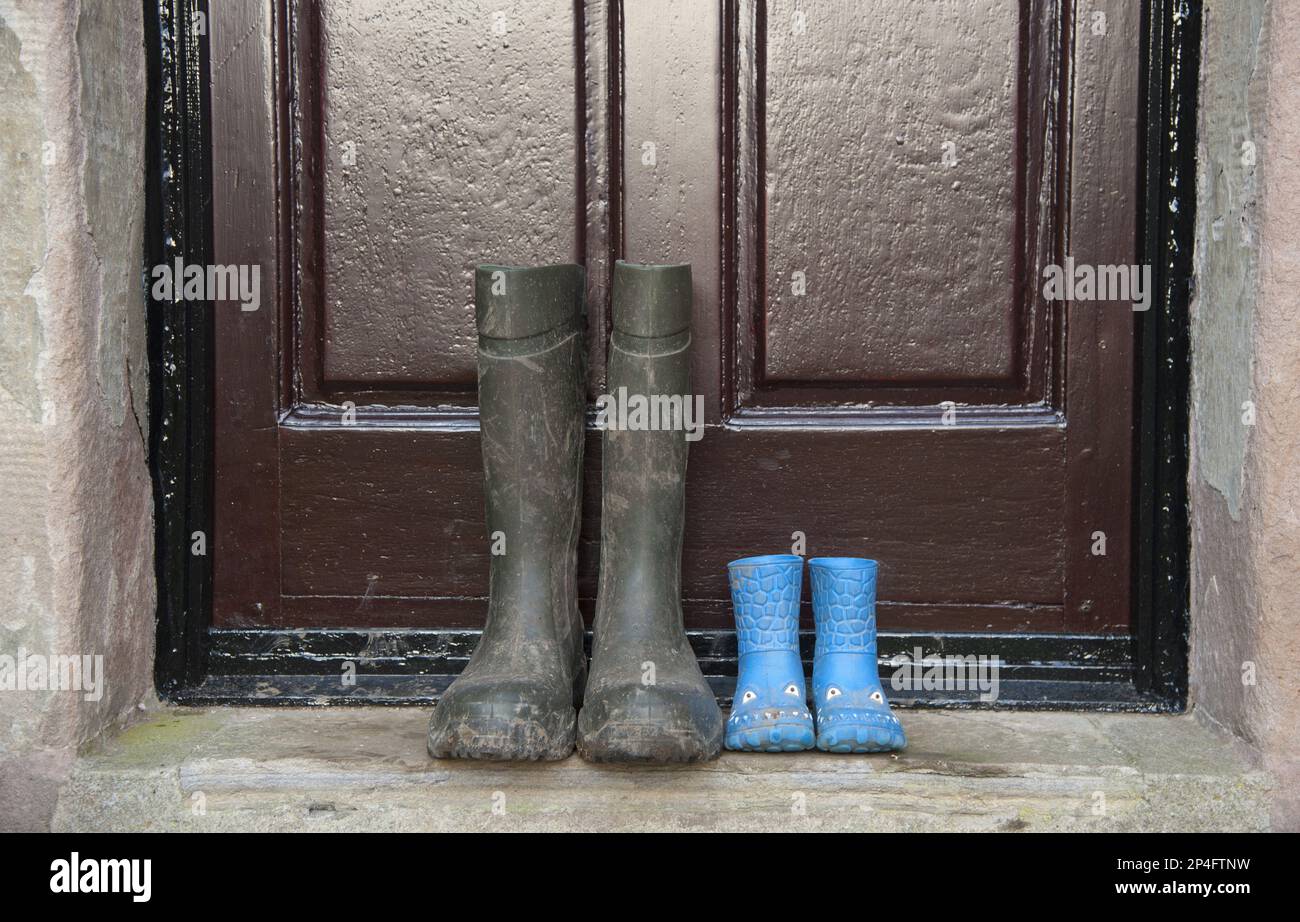 Due paia di wellies, un paio di stivali per bambini e un paio di stivali da uomo, fuori dalla porta della fattoria, Whitewell, Lancashire, England, United Foto Stock