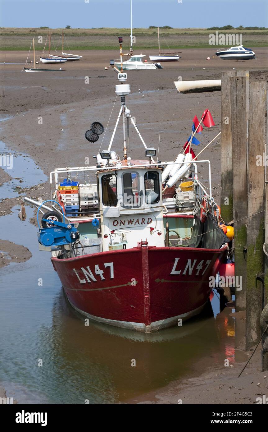 Barca da pesca ormeggiata al molo nel torrente costiero con bassa marea, Brancaster Harbour, Norfolk, Inghilterra, Regno Unito Foto Stock