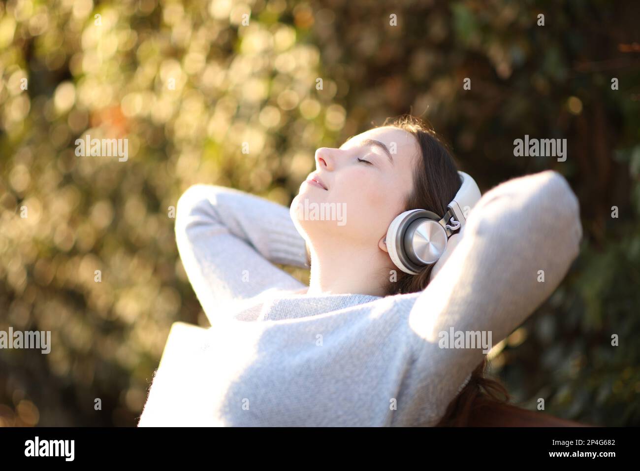 Donna che riposa ascoltando musica seduta su una panchina in un parco Foto Stock