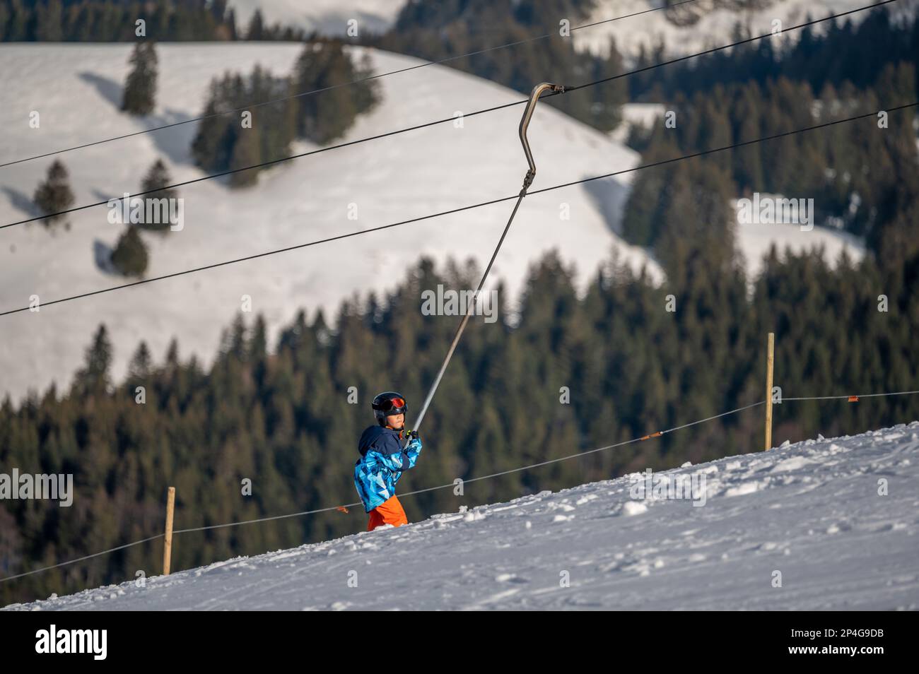 Sci per bambini sulla neve. Un ragazzo asiatico seduto sullo skilift afferrando la corda. Sport invernali. Les Pleiades, Svizzera. Foto Stock