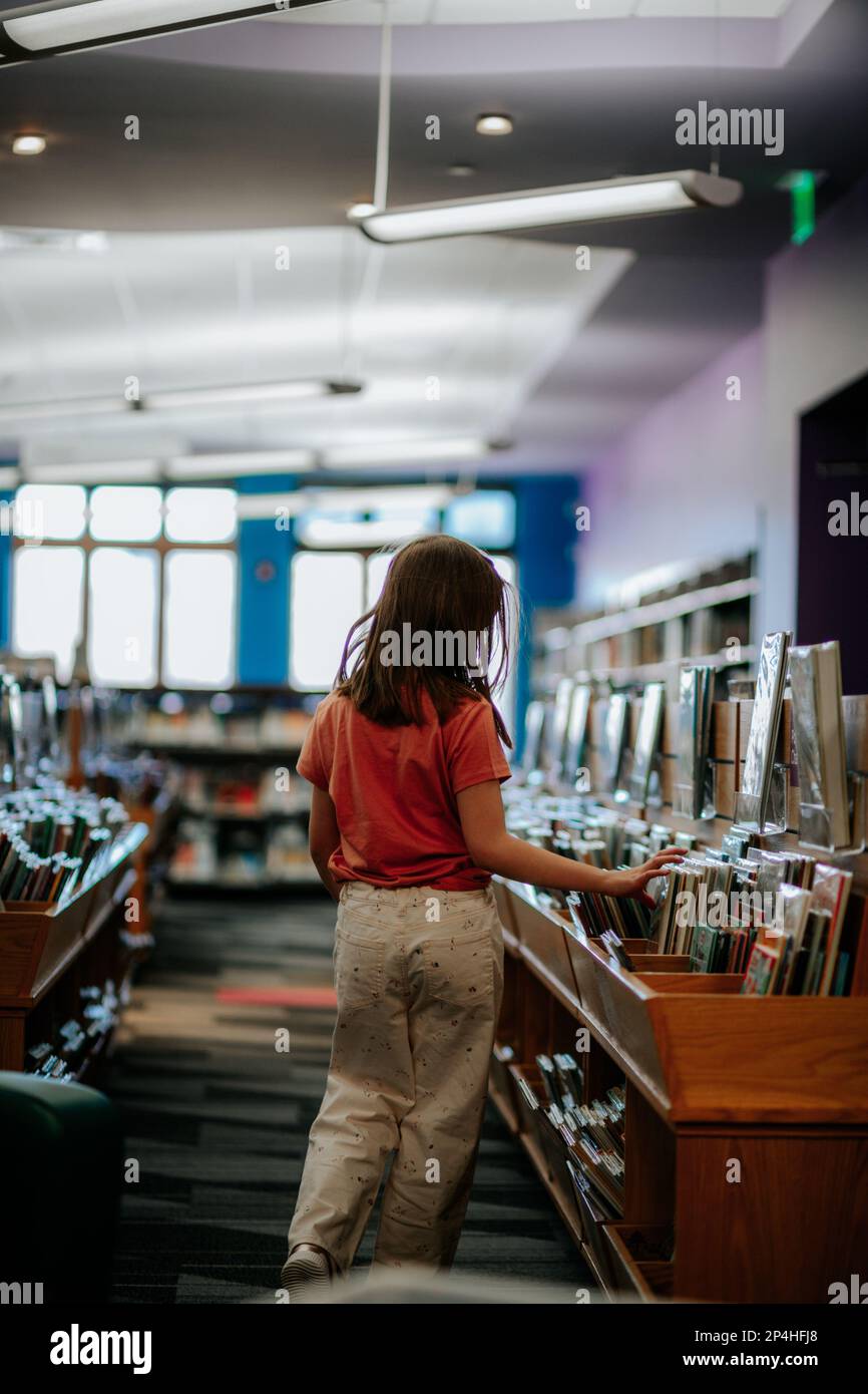 Ragazza giovane che raccoglie libri in una biblioteca Foto Stock