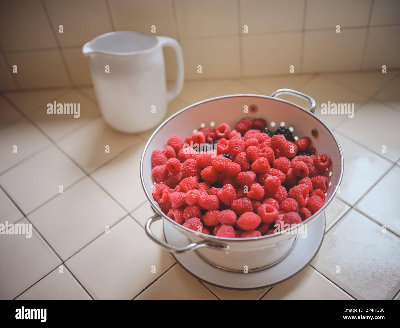 Lamponi in un colino con caraffa d'acqua sul bancone della cucina Foto Stock