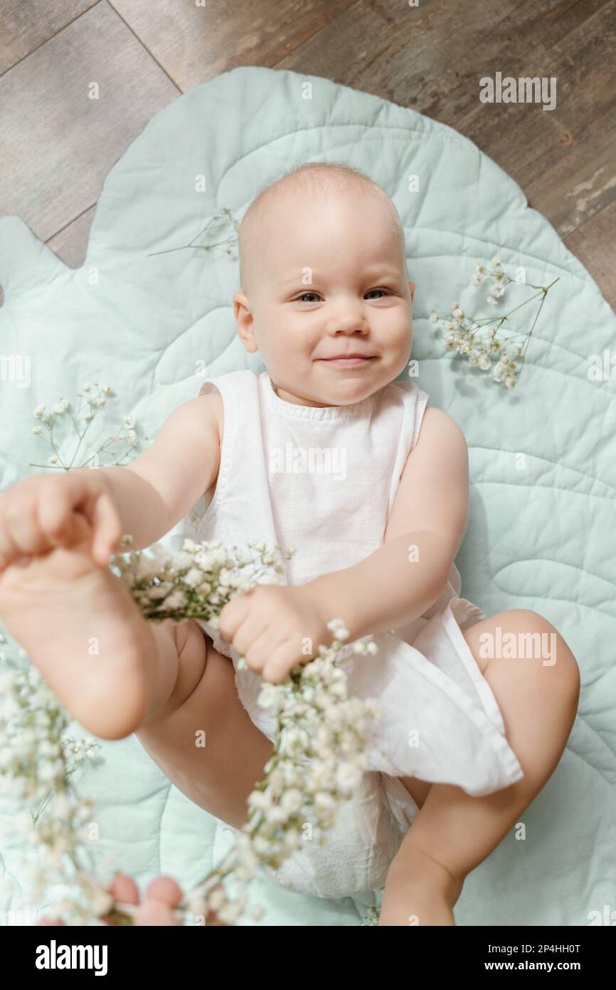 Bambina calva in un vestito di lino bianco con gypsofila su un tappeto di foglie Foto Stock