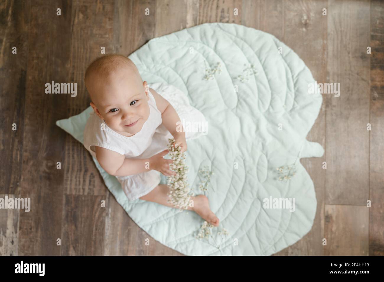 Bambina calva in un vestito di lino bianco con gypsofila su un tappeto di foglie Foto Stock