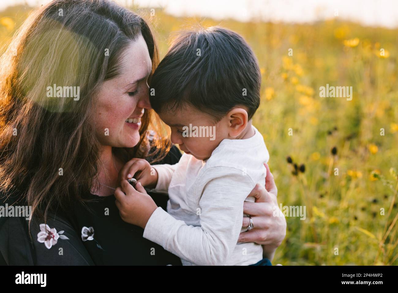 Mamma e figlio abbracciano alla luce del sole d'oro il giorno d'estate in campo di fiori Foto Stock