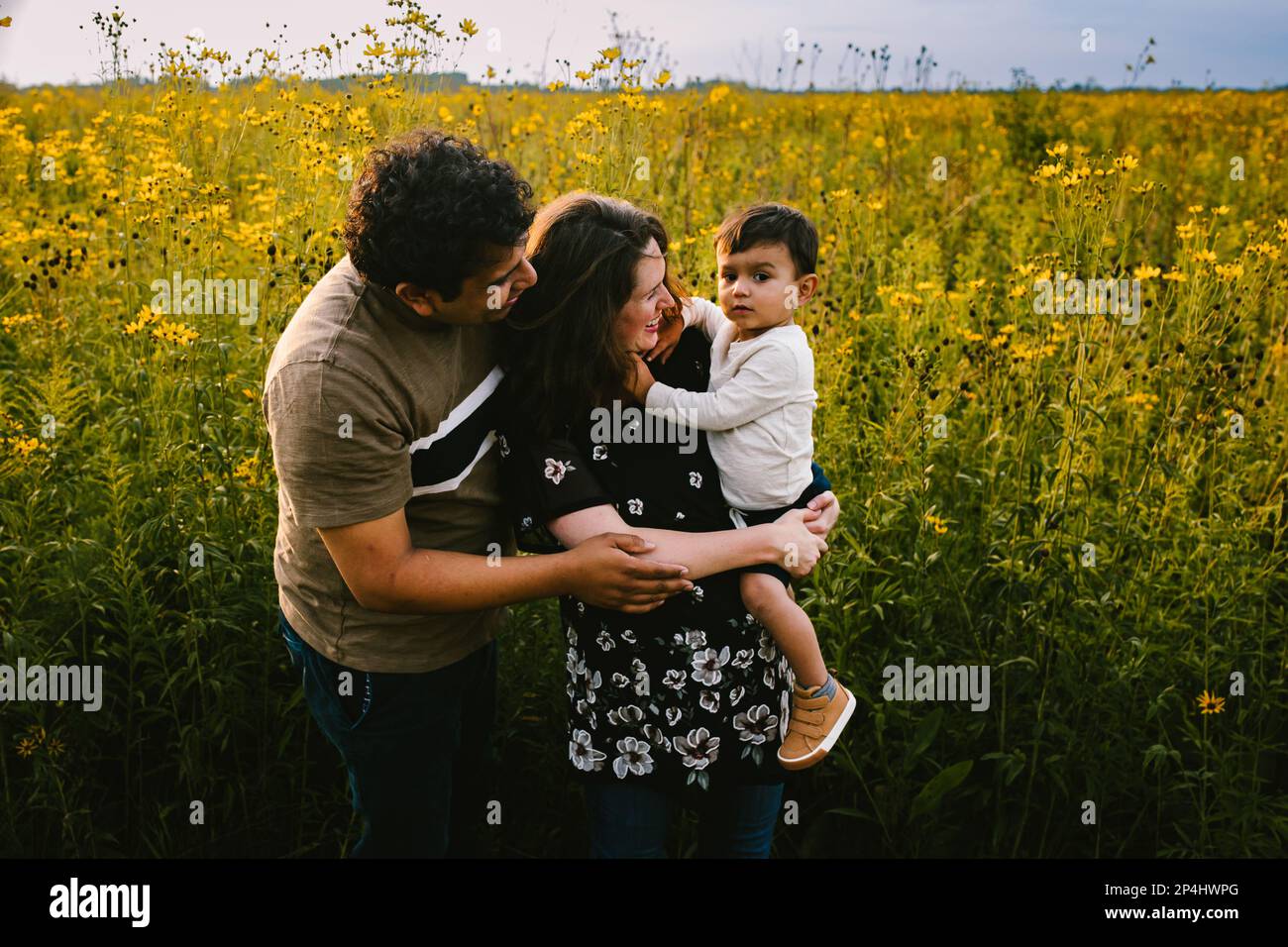 La famiglia multirazziale abbraccia il figlio del toddler davanti al campo di fiori selvaggi Foto Stock