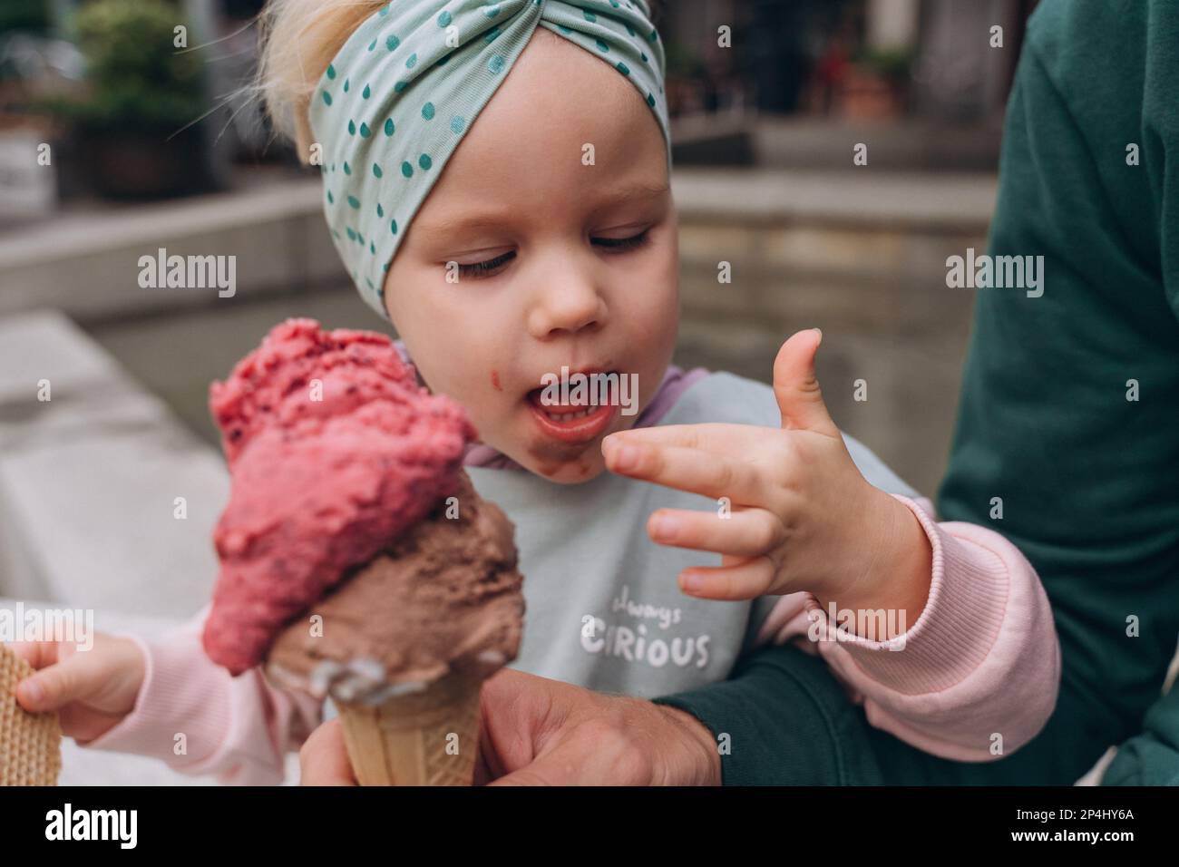 Una bambina sporca di gelato italiano le lecca le dita Foto Stock