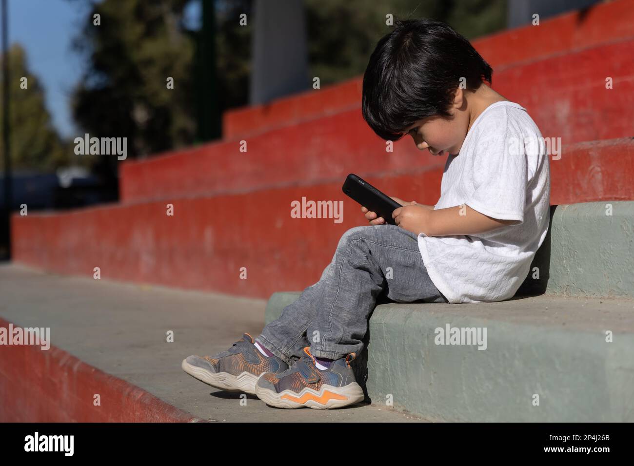 Bambino messicano che gioca con dispositivi mobili all'aperto Foto Stock