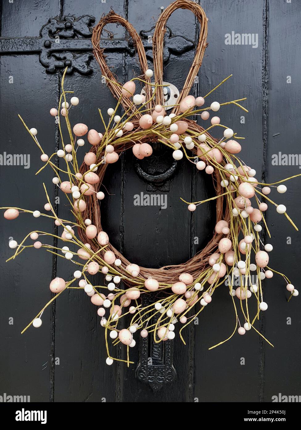 Una corona stagionale fatta di bacche rosa e bianche su una porta rivestita di pannelli scuri. Foto Stock