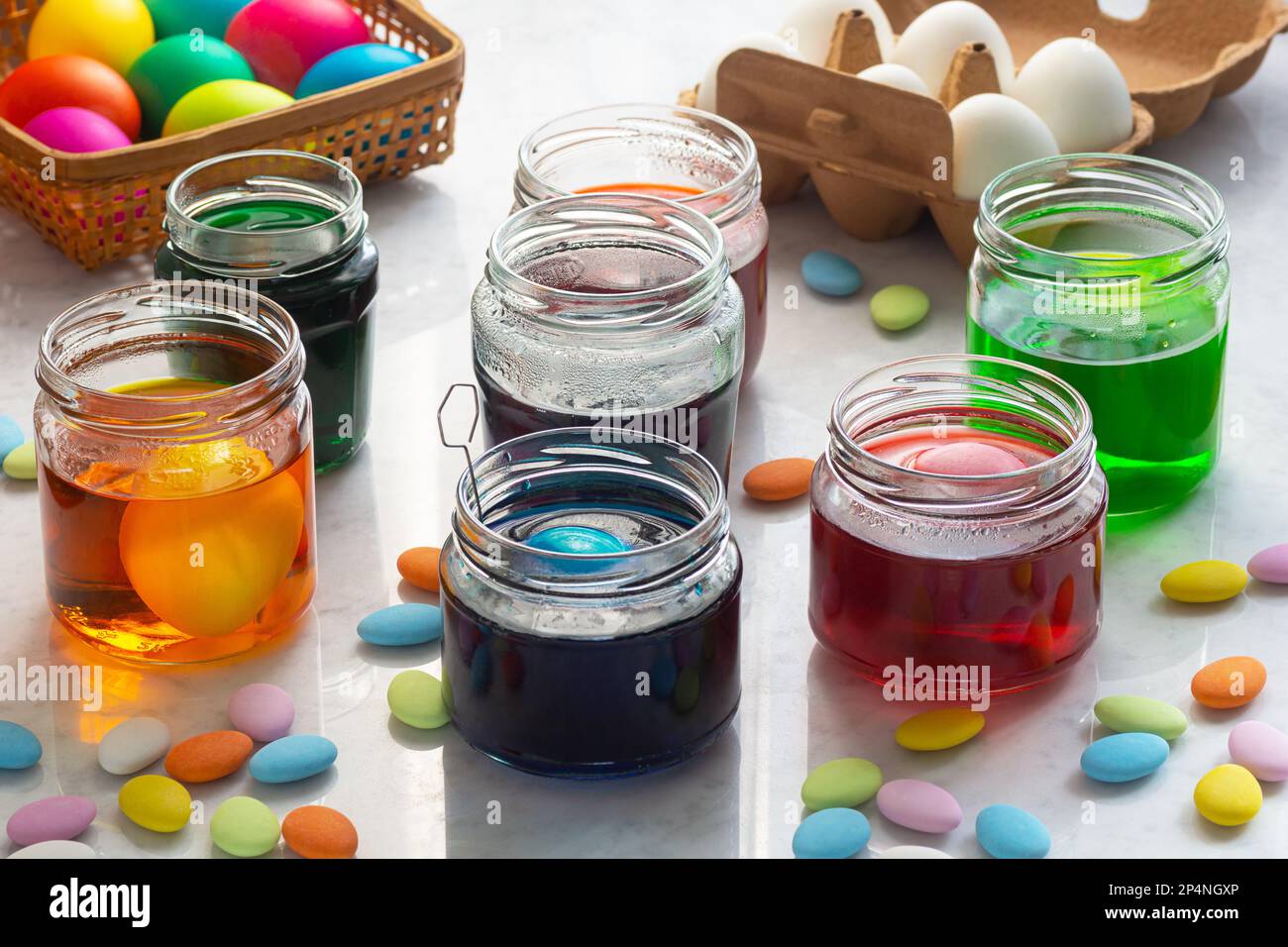 Tintura di uova di Pasqua in coloratissime tinte in vasetti di vetro con caramelle di Pasqua multicolore sul banco di marmo Foto Stock