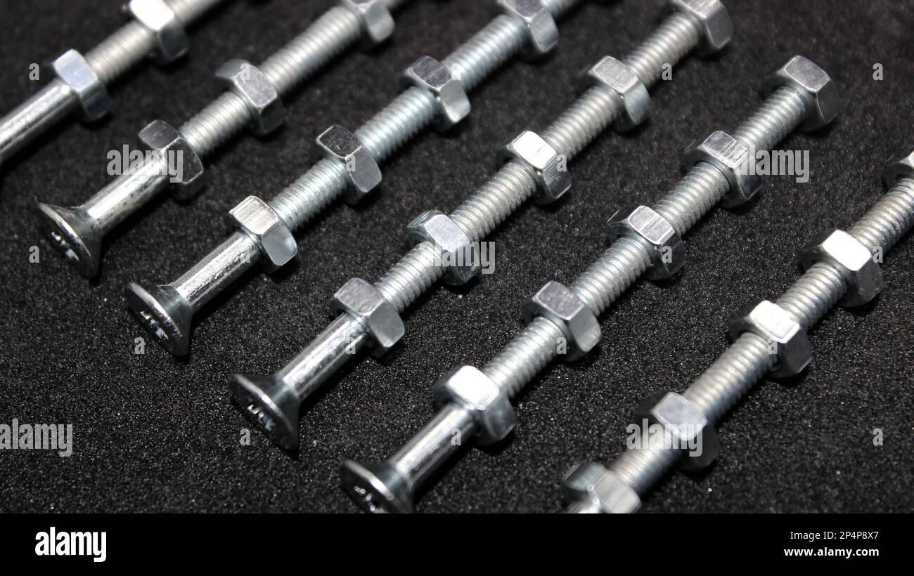 I dadi metallici sono avvitati in modo uniforme su bulloni lunghi filettati in file A su Una superficie nera Foto Stock