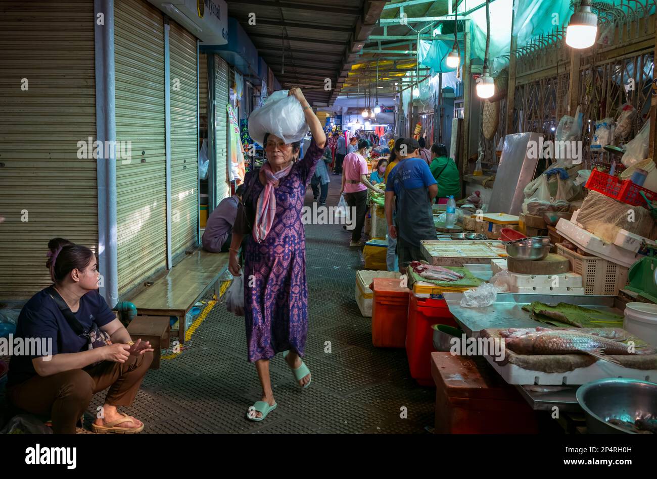 Una donna di mezza età trasporta un pacchetto sulla sua testa mentre cammina giù attraverso la sezione di pesce e frutti di mare del mercato centrale, Phnom Penh, Cambogia. Foto Stock