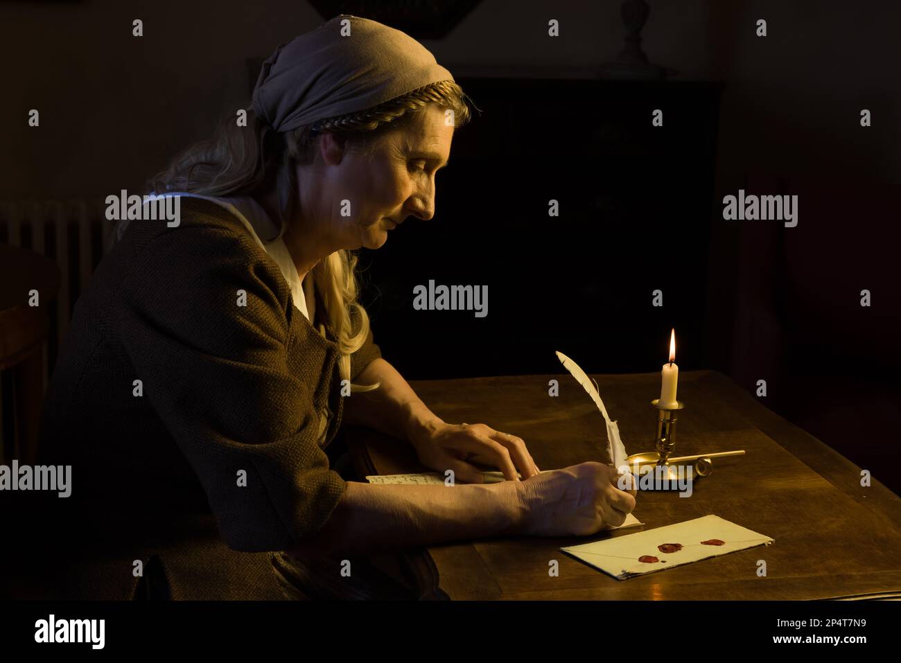 Signora in vestito medievale seduto in una stanza buia scrivendo una lettera con un piumino Foto Stock