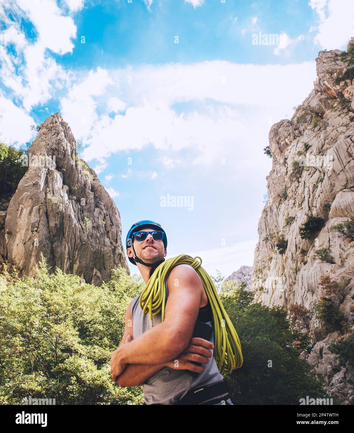 Ritratto di sorridente arrampicatore in casco protettivo e occhiali da sole con corda da arrampicata sulla spalla in piedi nel parco Paklenica tra roccia w rupe Foto Stock
