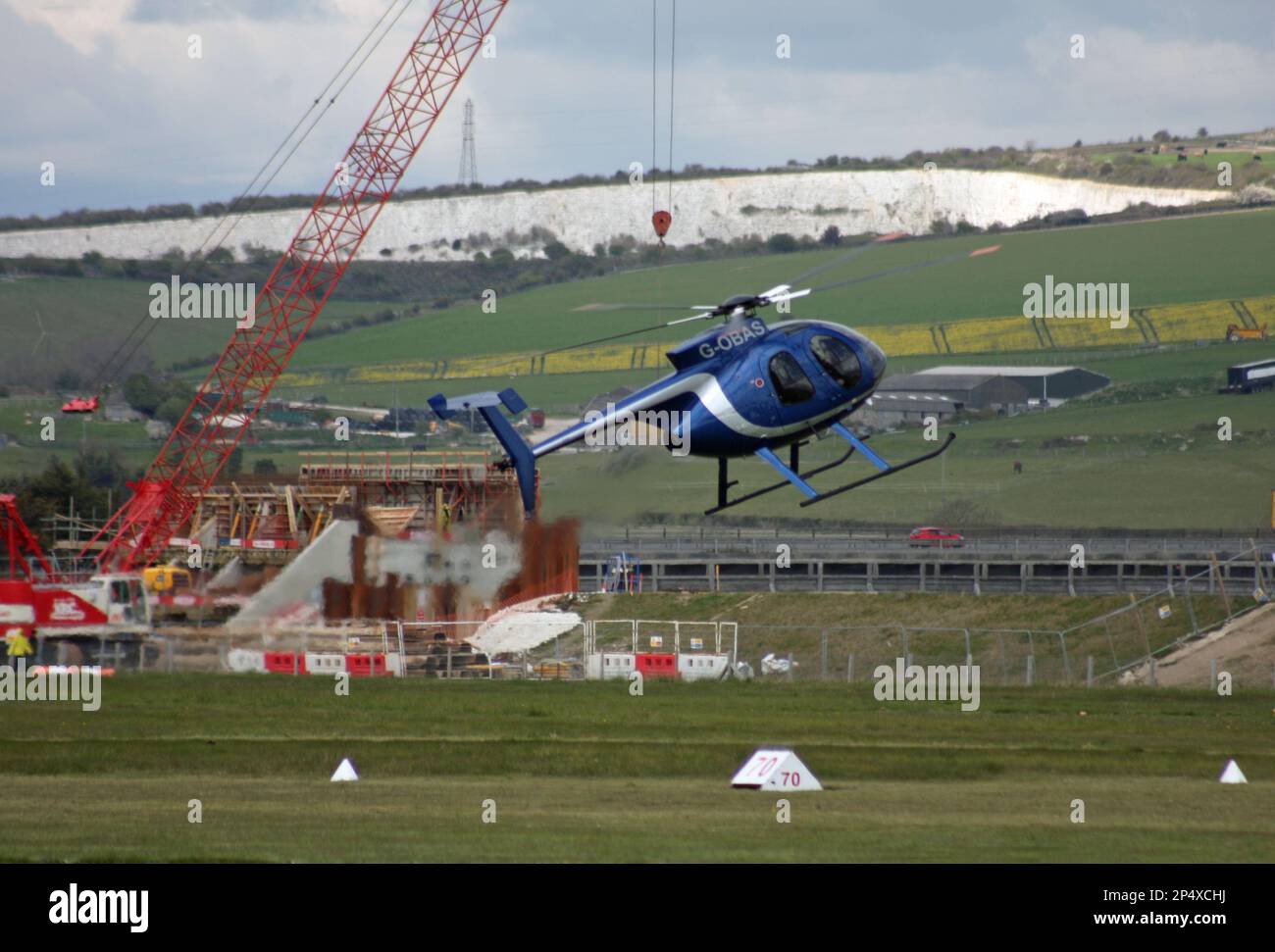 Un elicottero Hughes 369 manovra davanti ad una gru come se fosse caduta. Aeroporto di Brighton, Sussex, Inghilterra Foto Stock
