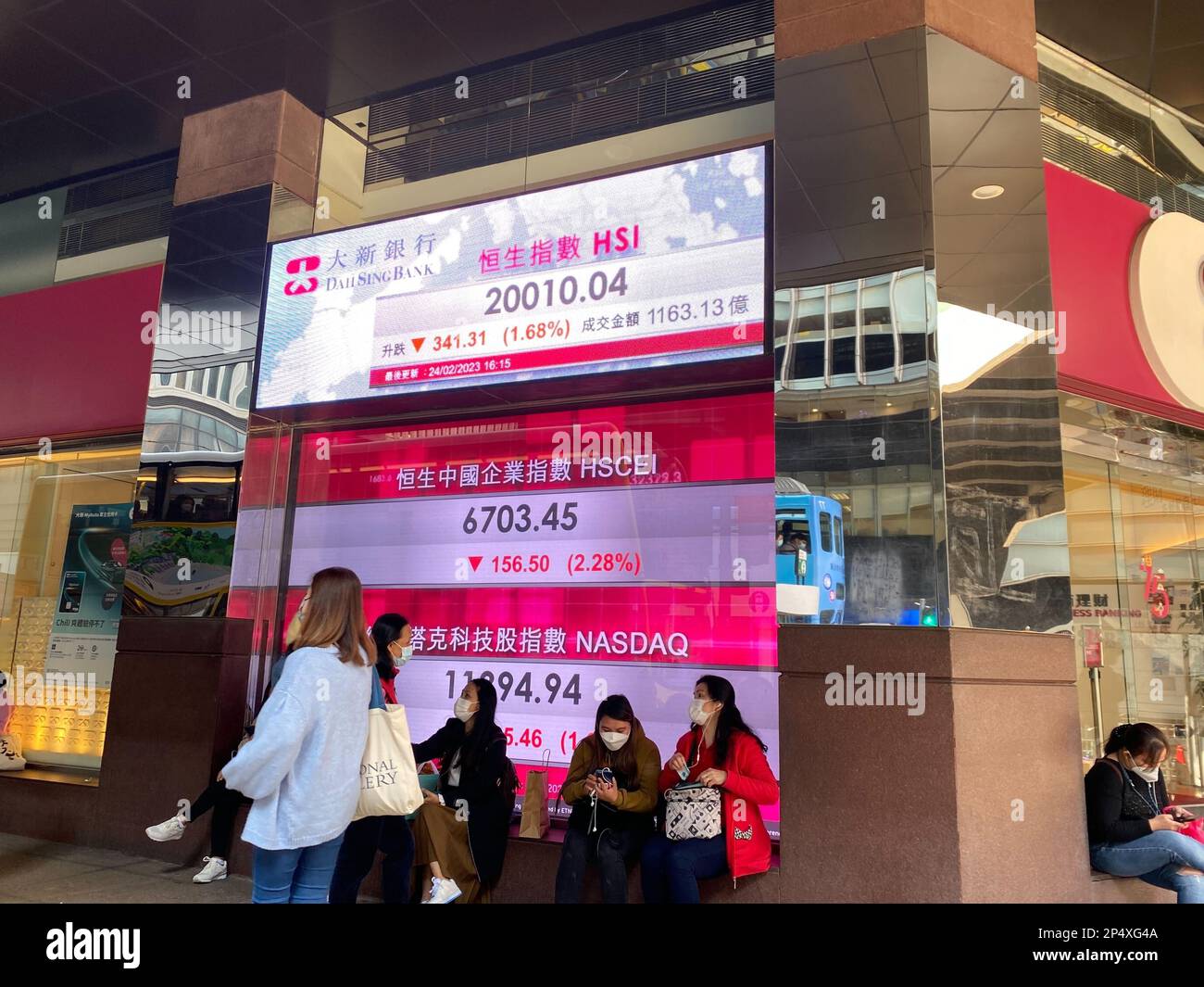 Persone che indossano maschere in piedi vicino a uno schermo che mostra gli indicatori del mercato azionario in centrale, Hong Kong. 24FEB23 Foto: Li Jiaxing Foto Stock
