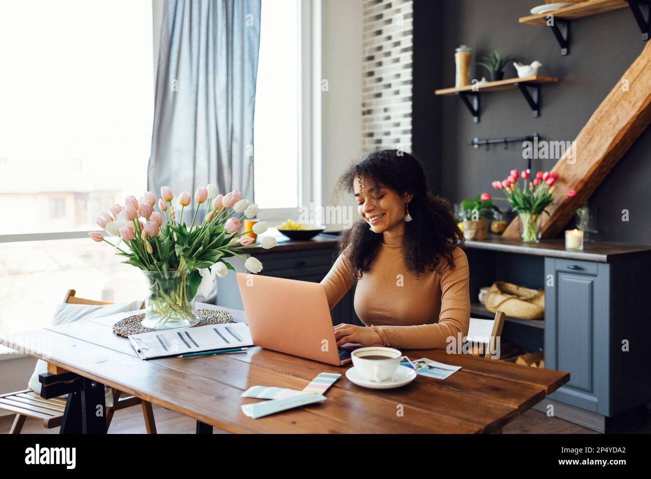 Felice giovane afro donna americana seduto a casa con un computer portatile e digitando sulla tastiera. Una studentessa sorridente o una freelance che guarda lo schermo del computer. Foto Stock