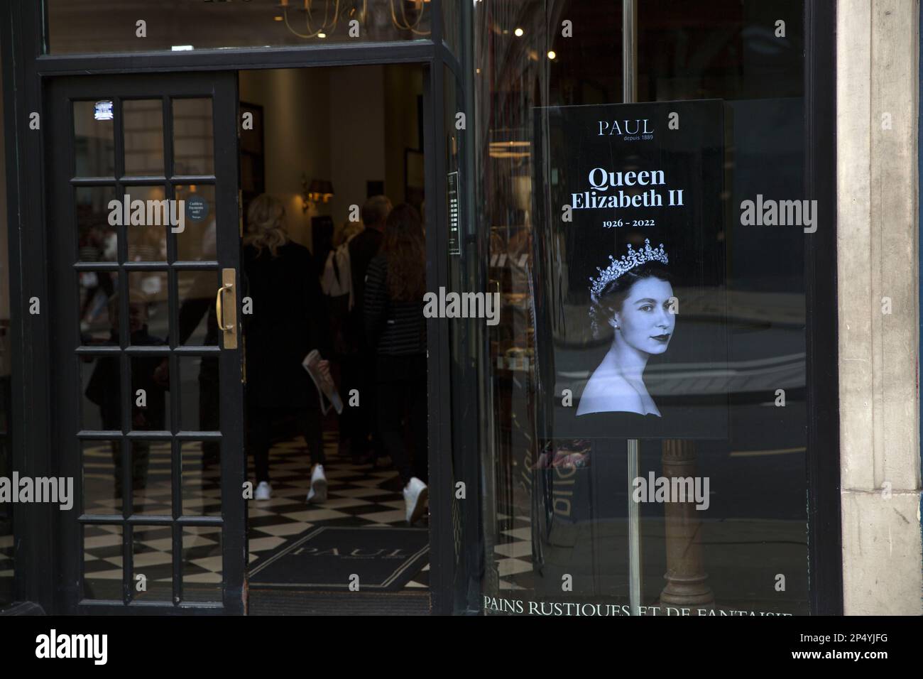 Un ritratto della defunto Regina Elisabetta II è visto come i lutto si riuniscono per rendere i loro rispetti nel centro di Londra, il giorno del suo funerale. Foto Stock