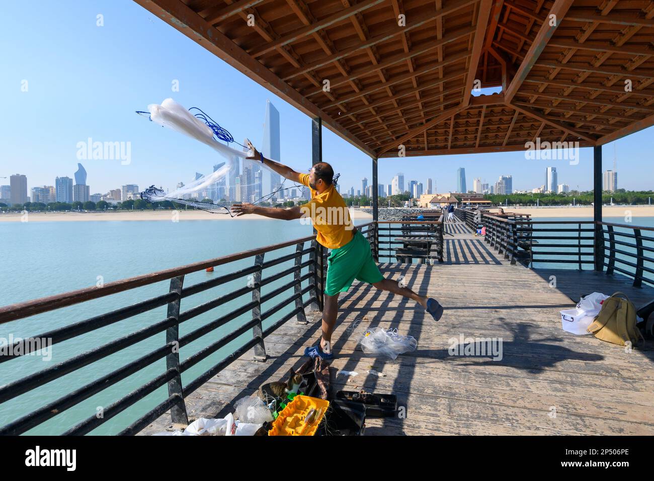 Uomini che pescano sulla rampa di pesca del Kuwait con lo skyline di Kuwait City dietro. indian fisher gettando la rete da un molo su Kuwai, Kuwait City, Medio Oriente. Foto Stock