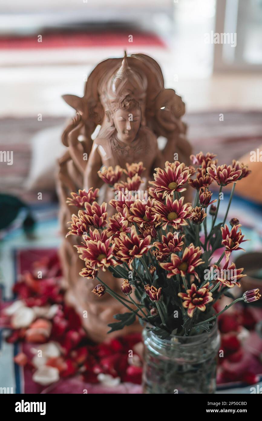Statua di Buddha in miniatura sul vaso da tavolo di fiori freschi in primo piano Foto Stock