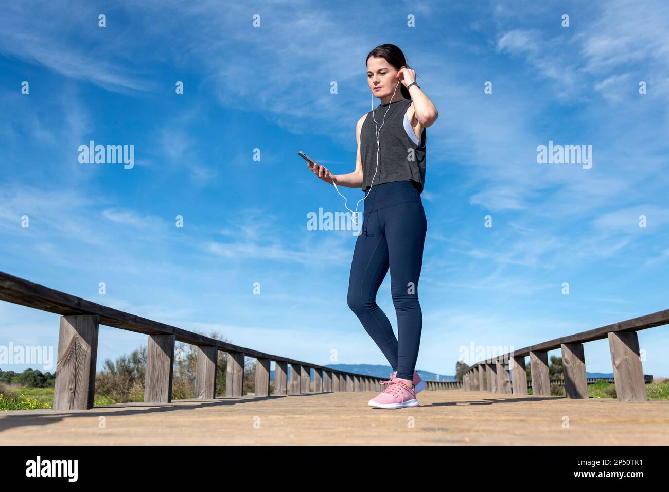 sportswoman regolare le sue cuffie durante una pausa di allenamento. Runner femminile che ascolta musica sugli auricolari durante le pause all'aperto. Foto Stock