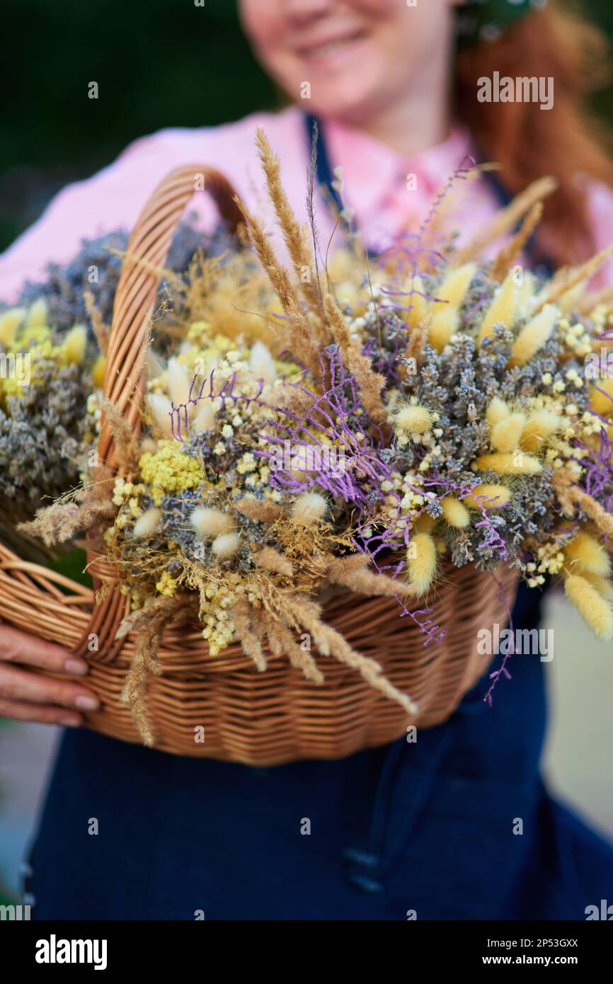 fattoria donna in grembiule con cesto di fiori secchi all'aperto, vita villaggio. Fiorista donna con grappoli di lavanda . Foto di alta qualità Foto Stock