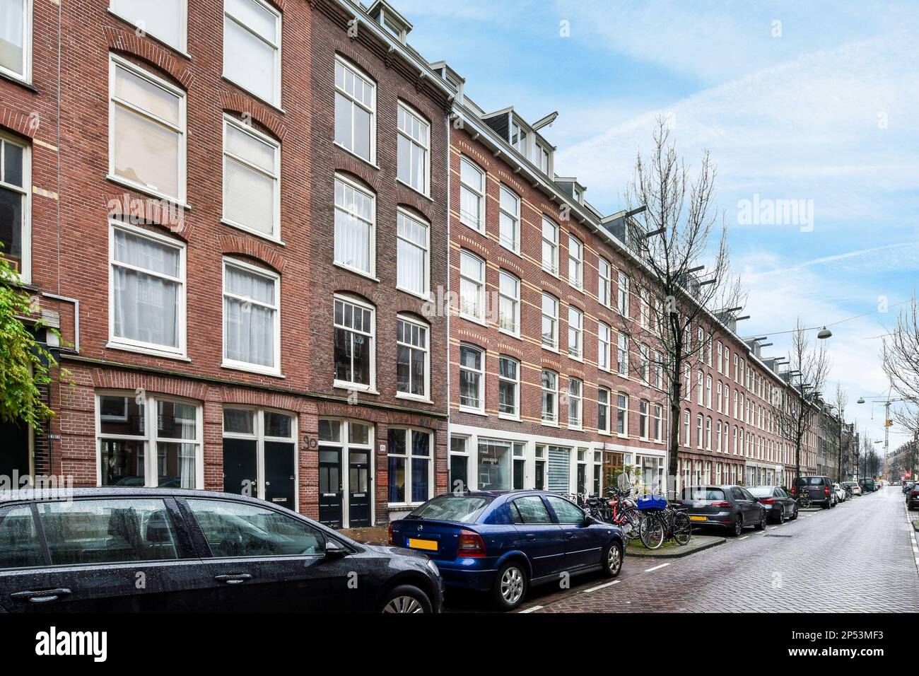 Amsterdam, Paesi Bassi - 10 aprile 2021: Alcune auto parcheggiate sul lato di una strada di fronte a una fila di edifici in mattoni con finestre bianche Foto Stock