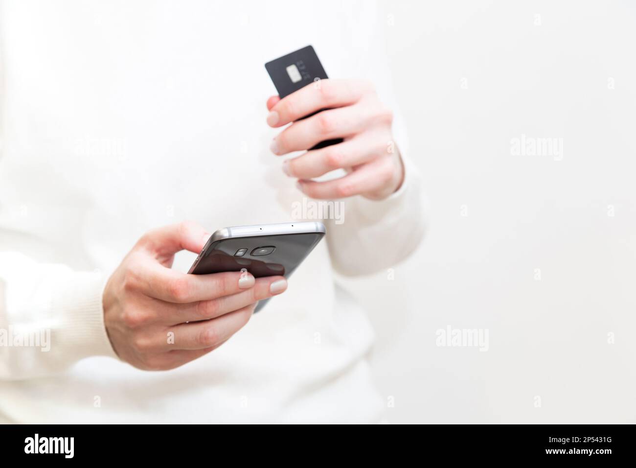 Primo piano delle mani femminili che tengono la carta di credito e utilizzano lo smartphone su sfondo bianco. Donna che paga in modo sicuro online, utilizzando il servizio bancario, ordinando i Foto Stock