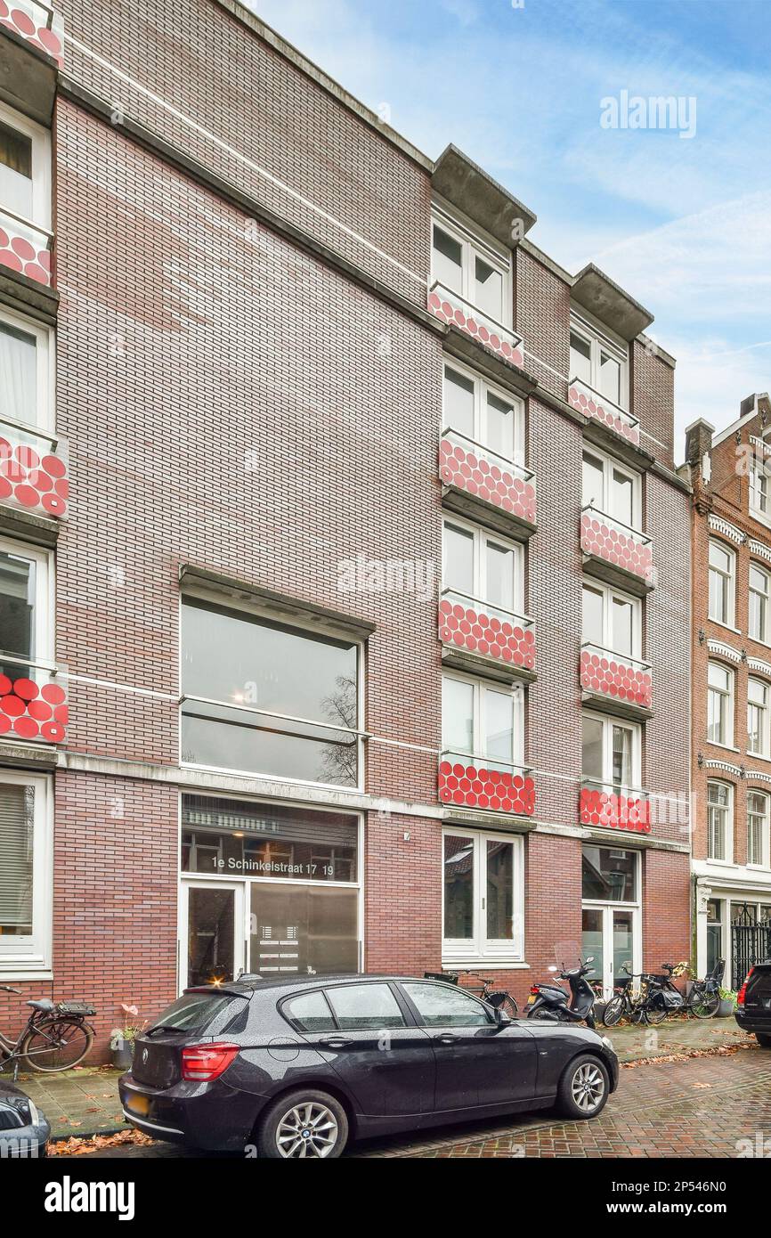 Amsterdam, Paesi Bassi - 10 aprile, 2021: Una strada cittadina con auto parcheggiate di lato e edifici dipinti in rosso, bianco e blu che sono stati vandalati Foto Stock