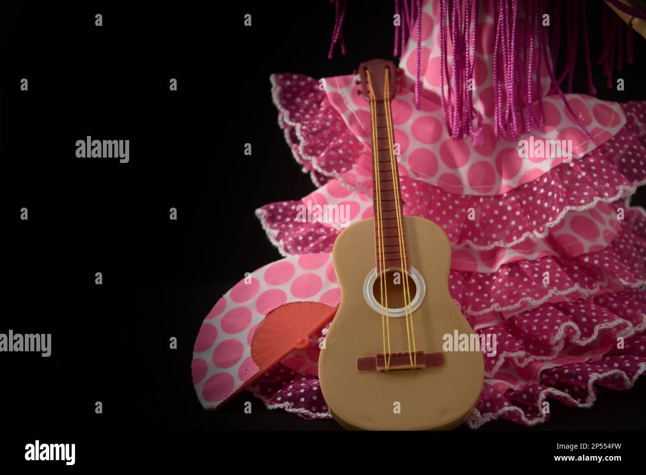 Immagine di un abito di flamenco o faralaes, accanto ad una chitarra e ad un fan degli stessi colori su sfondo nero con spazio copia Foto Stock