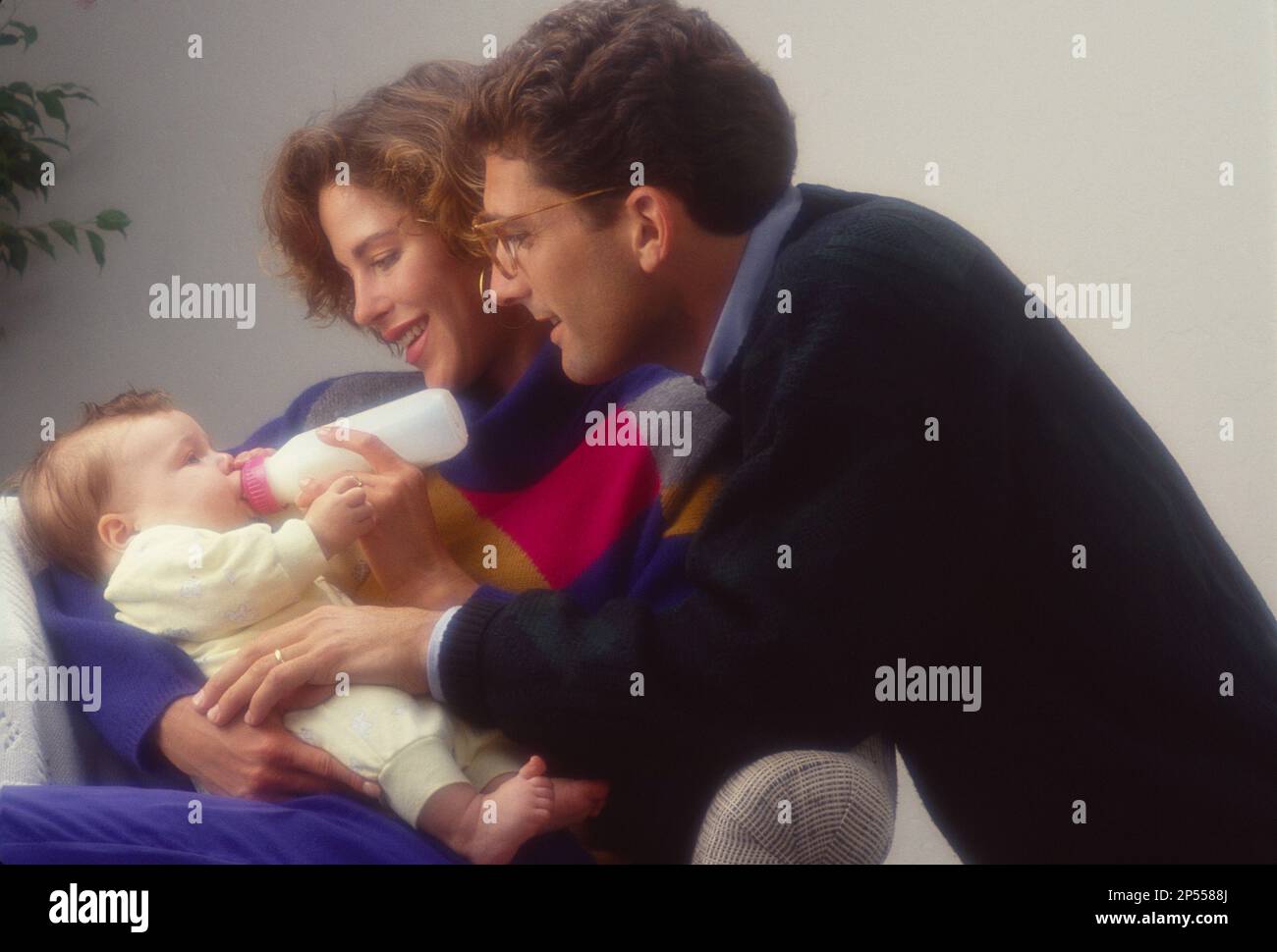 Marito e moglie più giovani con il loro bambino piccolo come suo bere una bottiglia di latte Foto Stock