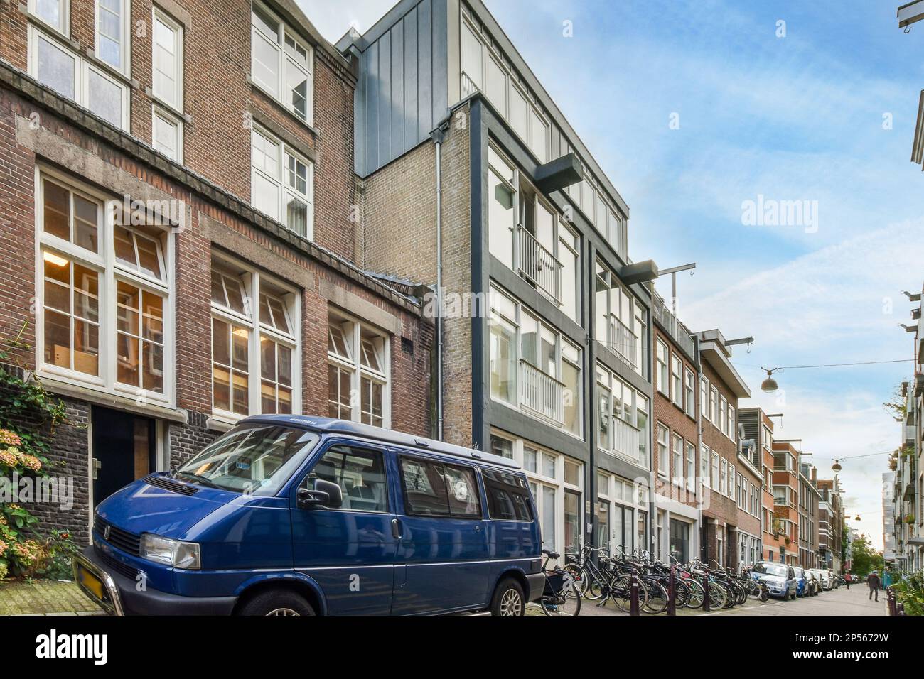 Amsterdam, Paesi Bassi - 10 aprile 2021: Un furgone blu parcheggiato sul lato di una strada di fronte a una fila di alti edifici in mattoni con finestre bianche Foto Stock