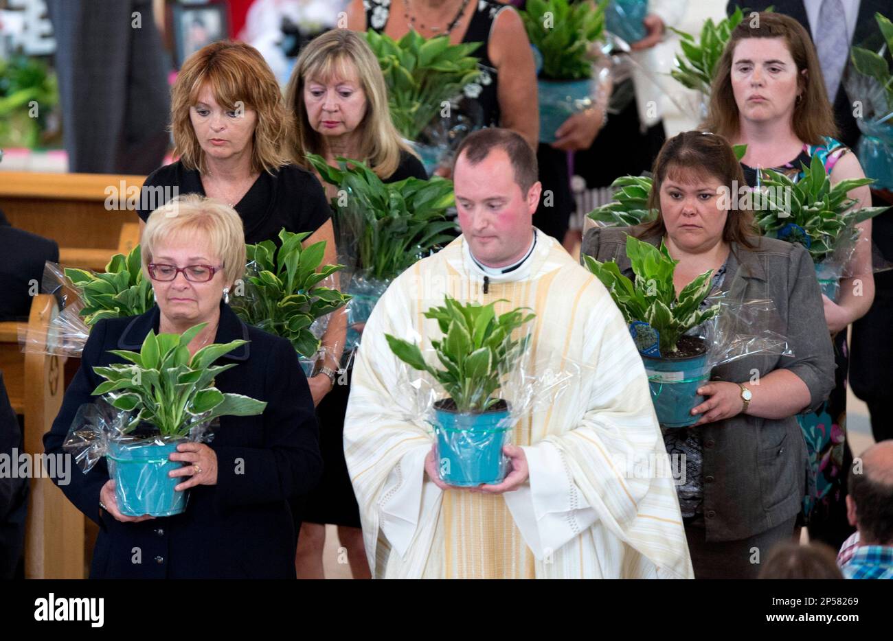 Mayor Colette Roy-Laroche, left, Father Steve Lemay and volunteers carry plants to offer the families of the victims during a memorial service on Saturday, July 27, 2013, for the victims killed when a runaway oil train derailed and exploded in Lac-Megantic, Quebec. The service was held three weeks after a runaway train carrying crude oil careened off the tracks and exploded into a fireball, devastating the town of 6,000. (AP Photo/The Canadian Press, Paul Chiasson) Foto Stock