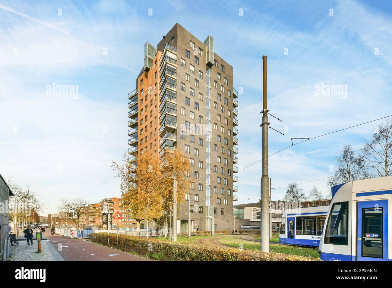 un treno sui binari di fronte ad un edificio di appartamenti con un tram blu e bianco parcheggiato accanto ad esso Foto Stock