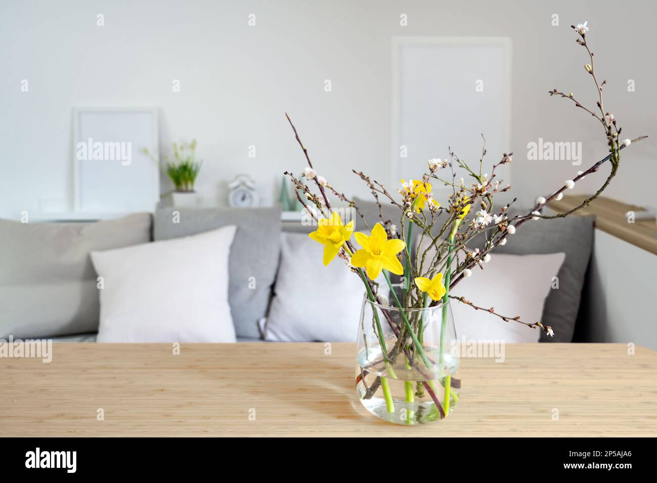 Bouquet primaverile con daffodils e rami fioriti in vaso di vetro su un tavolo di fronte a una panca divano, arredamento stagionale, spazio copia, selezionato fo Foto Stock