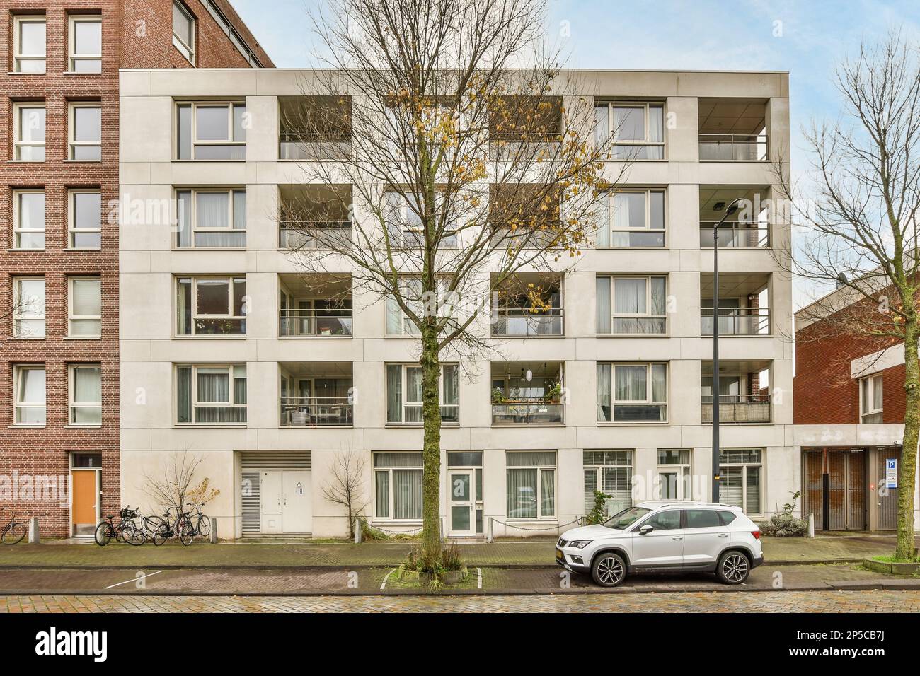 Amsterdam, Paesi Bassi - 10 aprile 2021: Un'auto bianca parcheggiata di fronte a un edificio con molte finestre e balle sul lato della strada Foto Stock