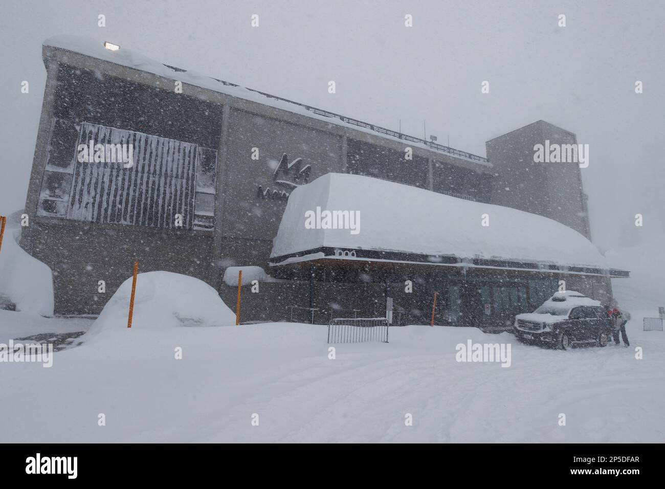 La neve profonda si accumula sul tetto del Canyon Lodge durante un blizzard invernale presso la stazione sciistica di Mammoth Mountain nelle montagne orientali della Sierra Nevada. Foto Stock