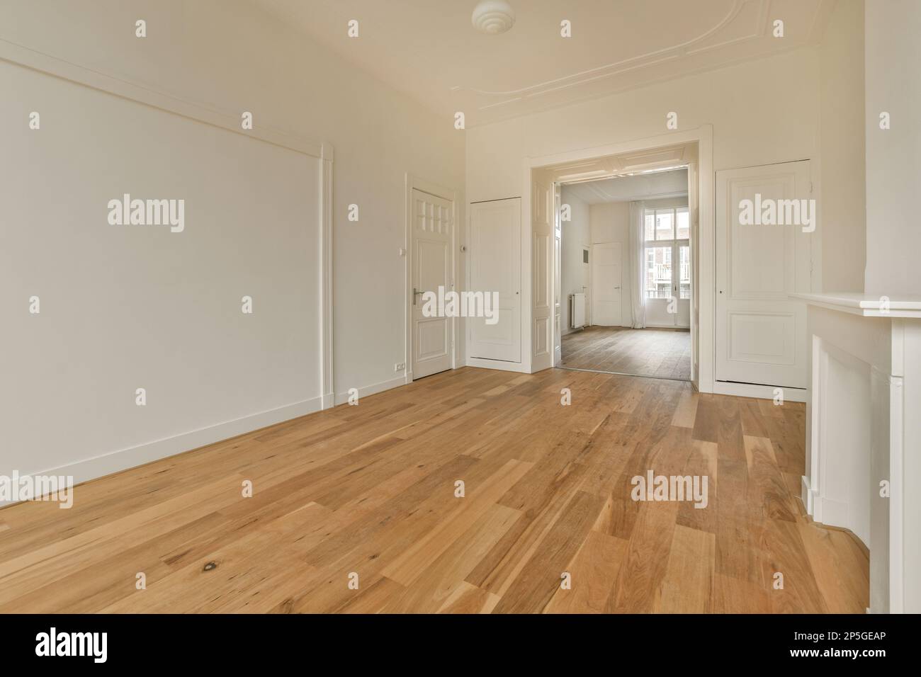 un soggiorno vuoto con pavimenti in legno duro e rifiniture bianche sulle pareti c'è una porta che conduce ad un'altra stanza Foto Stock