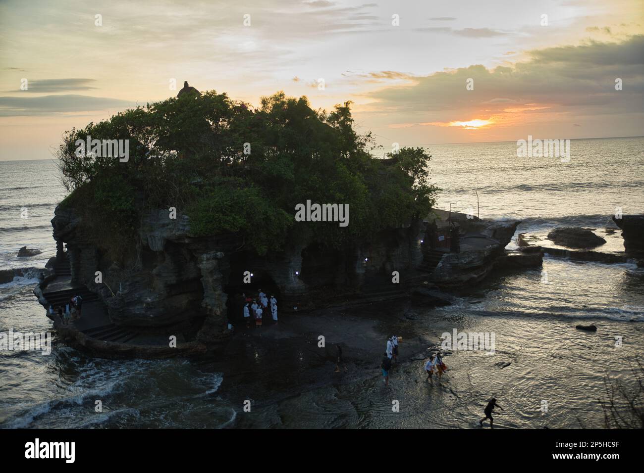 Foto di tutto il tempio di pura Tanah Lot, preso dall'alto completamente circondato dal mare, con un cielo tramonto sullo sfondo. Foto Stock