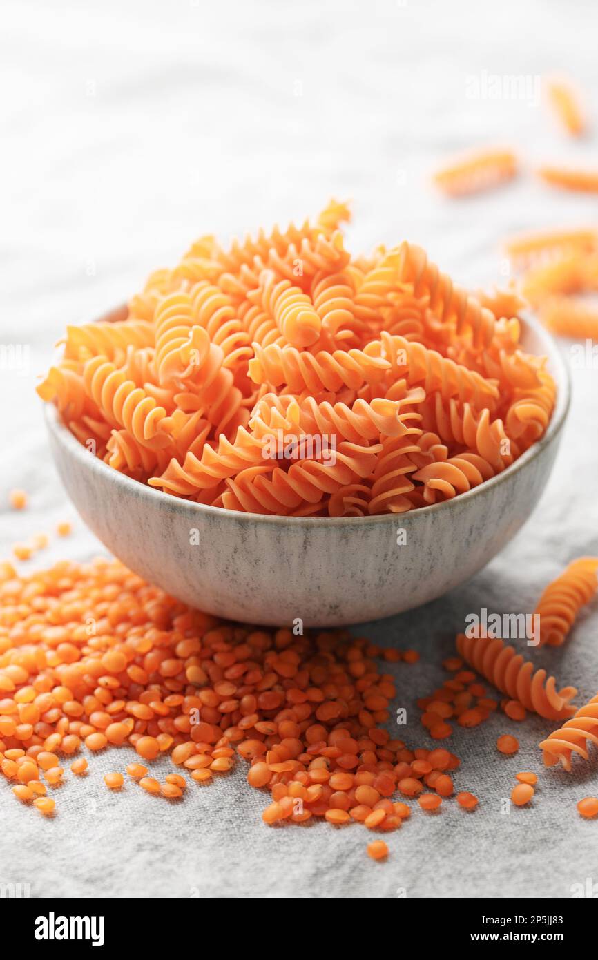 Lenticchie rosse fusilli su fondo tessile grigio. Ciotola con pasta cruda e lenticchie rosse. Pasta senza glutine. Foto Stock