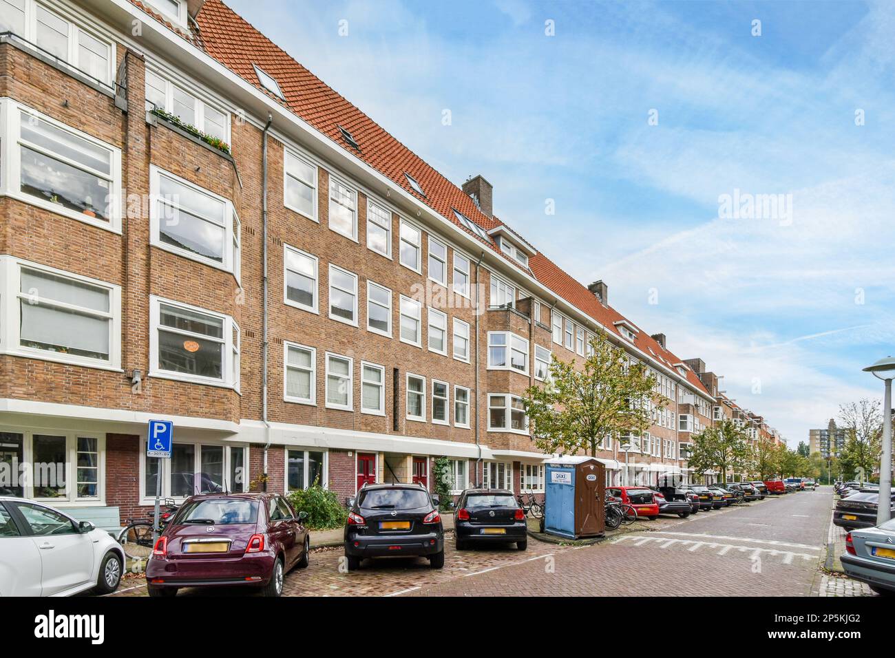 Amsterdam, Paesi Bassi - 10 aprile 2021: Alcune auto parcheggiate sul lato di una strada di fronte a una fila di edifici in mattoni con finestre bianche Foto Stock