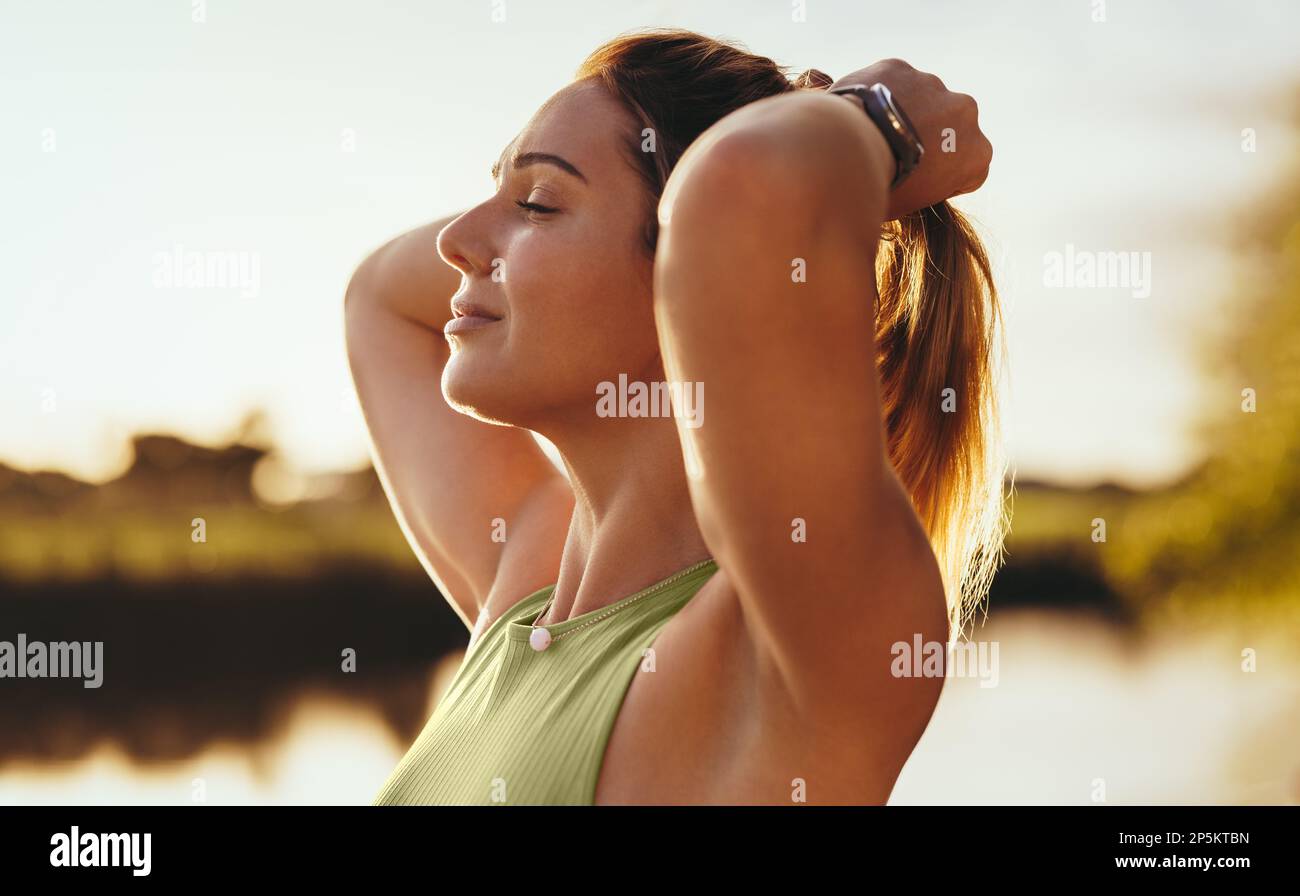 Donna che fa un esercizio di respirazione all'aperto al mattino. Donna serena meditare mentre si trova accanto ad un lago. Praticare lo yoga e una sana vita Foto Stock