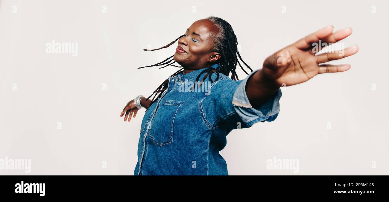 Felicità matura. Donna spensierata con lucchetti in piedi con gli occhi chiusi e le braccia distese. Allegra donna di mezza età che indossa un denim j Foto Stock