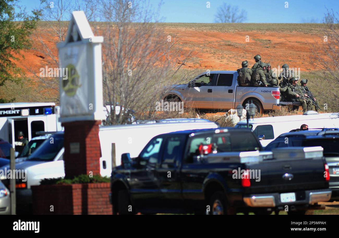 Law enforcement personnel in tactical gear ride a pickup to the scene