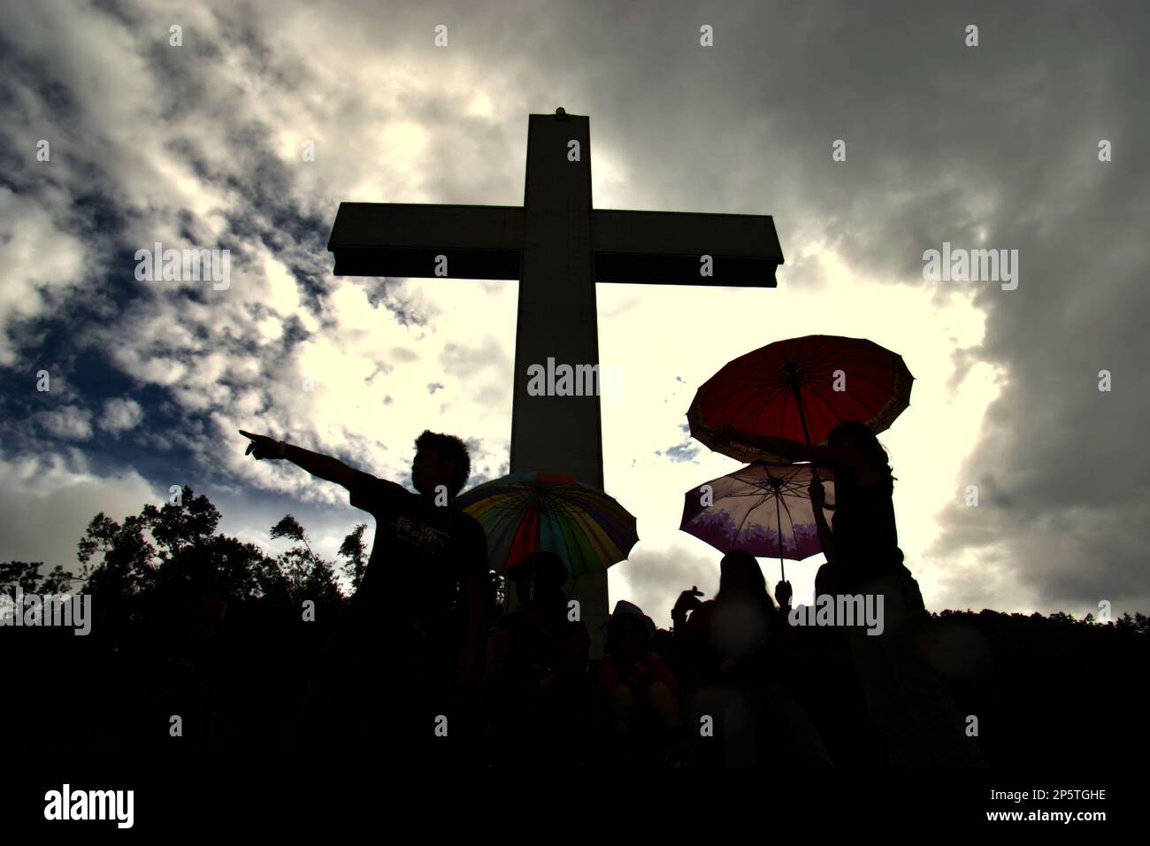 Silhouette di visitatori e un'alta croce cristiana a Bukit Kasih (collina dell'amore), una popolare destinazione turistica religiosa situata nel villaggio di Kanonang, Kawangkoan occidentale, Minahasa, Nord Sulawesi, Indonesia. Dedicato a tutti i credenti e devoti, promuovendo gli spiriti dell'amore, della pace e della tolleranza; Bukit Kasih fu iniziato all'inizio del 2000, quando Adolf J. Sondakh fu il governatore della provincia di Sulawesi settentrionale. Fu considerata una nobile iniziativa di pace; una risposta ai conflitti basati sulla religione e l'etnicità avvenne prima e intorno al 2000 in diverse altre province. Foto Stock