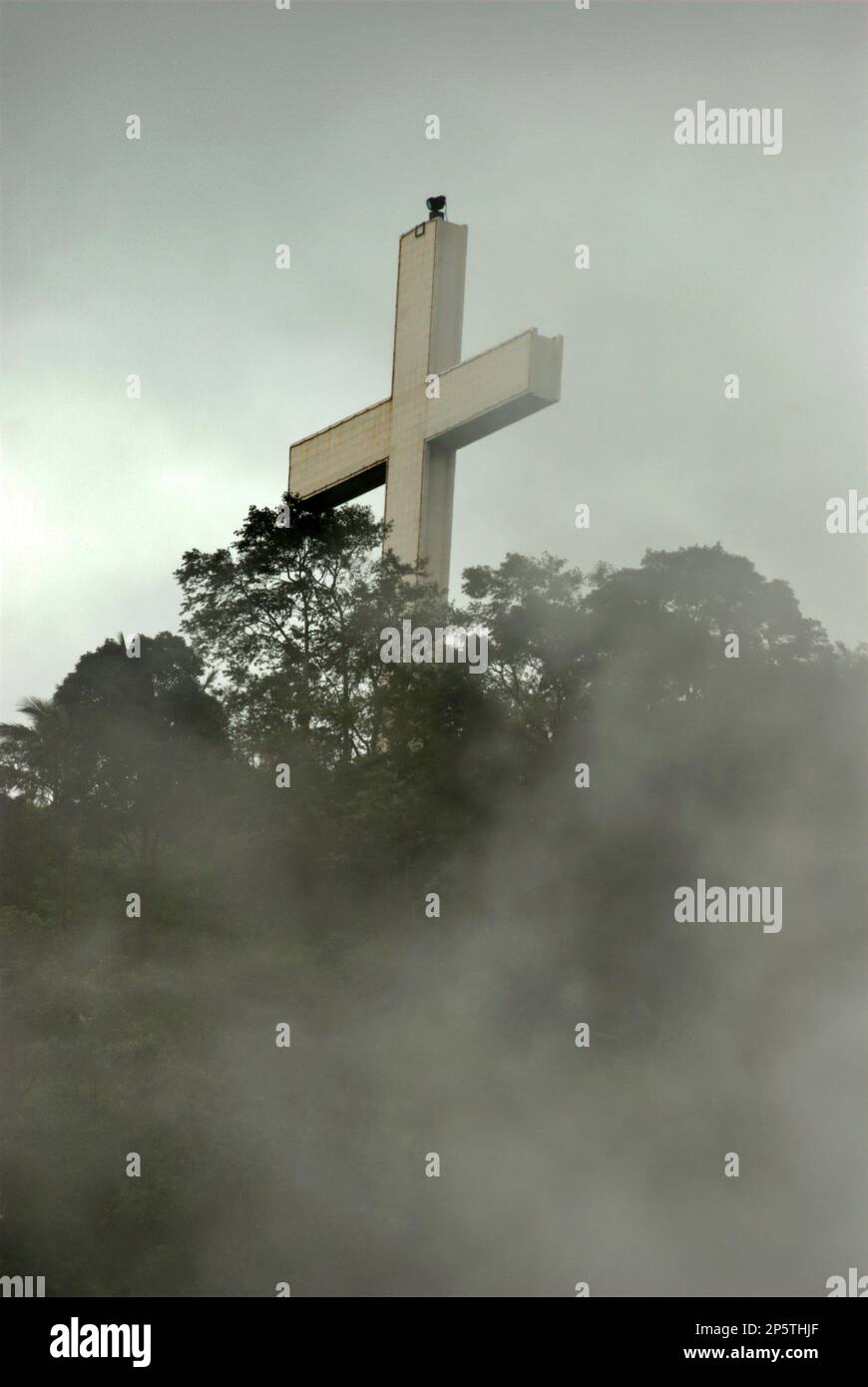 Un'alta croce cristiana emerge attraverso la nebbia su una cresta che conduce alla cima piatta del Bukit Kasih (collina dell'amore), dove sono stati costruiti siti di culto che rappresentano tutte le religioni ufficialmente riconosciute in Indonesia. Situato nel villaggio di Kanonang, West Kawangkoan, Minahasa, North Sulawesi, Bukit Kasih è una popolare destinazione turistica religiosa. dedicato ai credenti religiosi e ai devoti di tutte le fedi, Bukit Kasih è stato costruito nei primi anni '2000 durante l'amministrazione di Adolf J. Sondakh come governatore del Sulawesi settentrionale. E' stata concepita come una nobile iniziativa di pace. Foto Stock