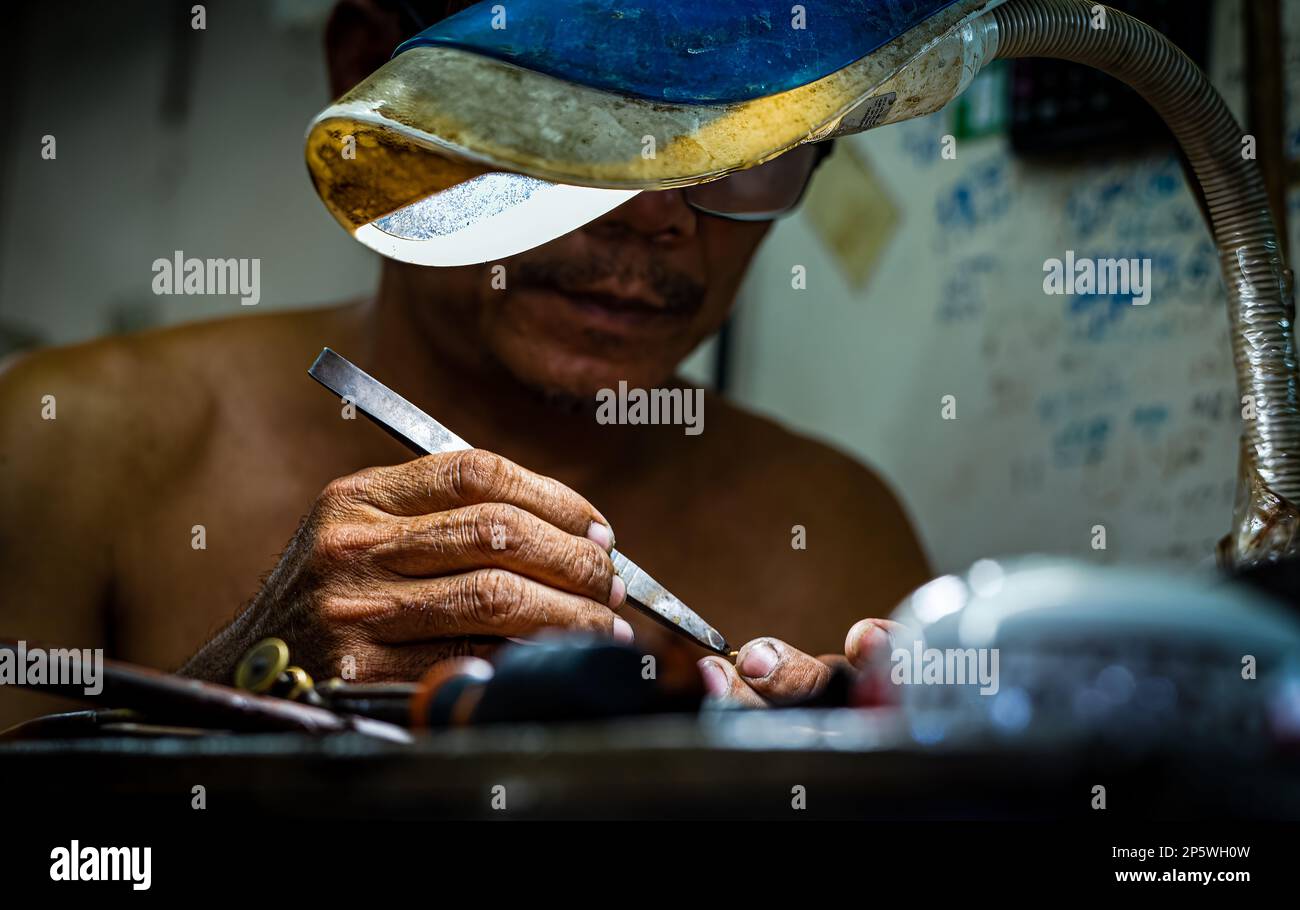 Un primo piano delle mani e delle pinzette di un gioielliere e orafo che lavora su un pezzo d'oro all'interno del mercato centrale a Phnom Penh, Cambogia. Foto Stock