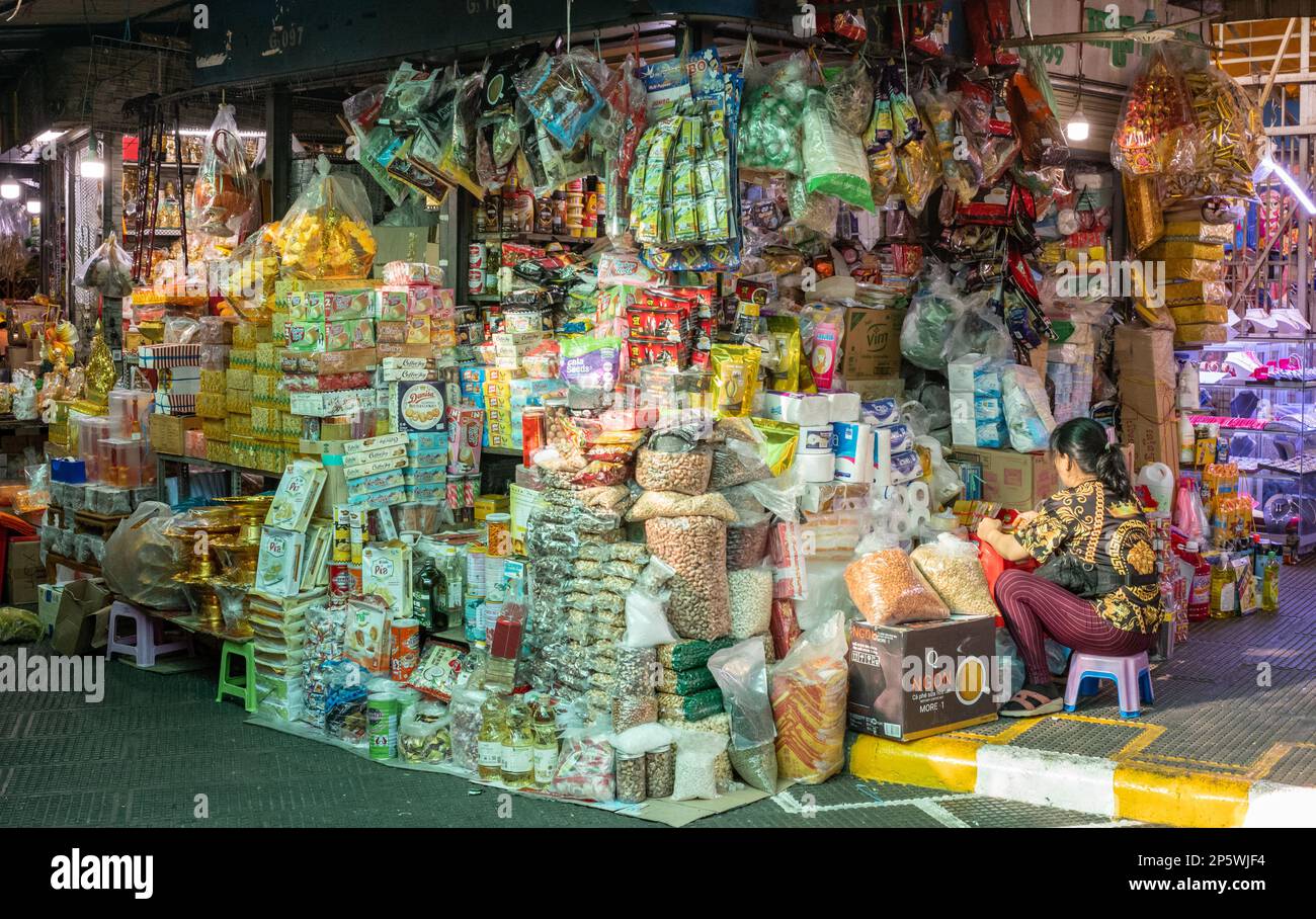 Una donna si siede accanto alla sua stalla che vende generi alimentari e articoli per la casa in generale nel mercato centrale a Phnom Penh, Cambogia. Foto Stock